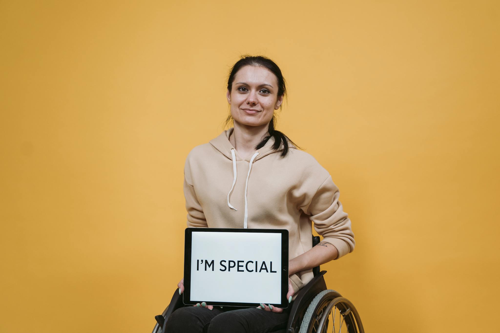 A confident woman in a wheelchair holding a sign with the message 'I'm special' against a yellow background.